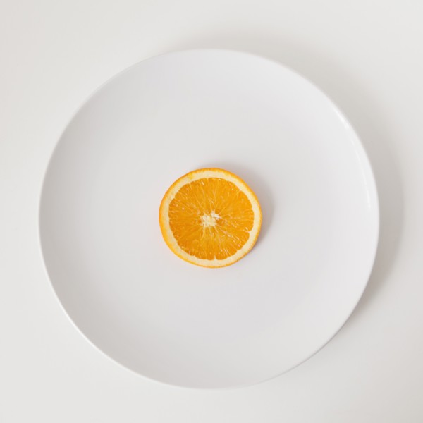 Slice of orange on plate, studio shot. 
Photo : Jessica Peterson