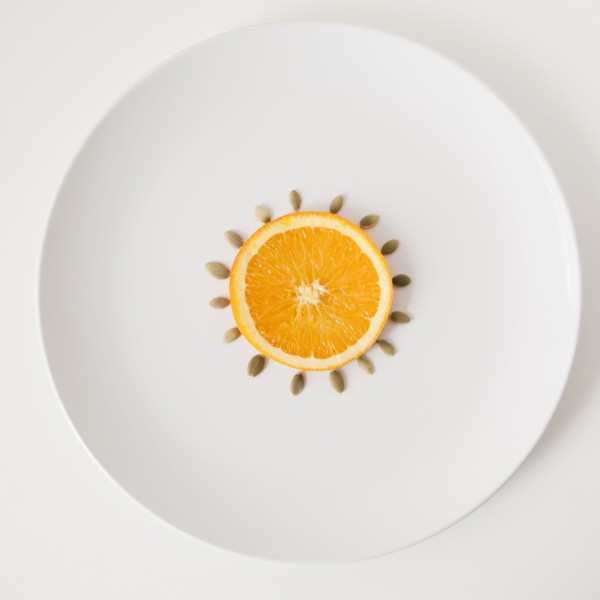 Slice of orange and seeds on plate, studio shot. 
Photo : Jessica Peterson