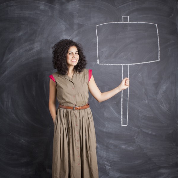 Young teacher posing against blackboard with blank banner written in chalk. 
Photo : Jessica