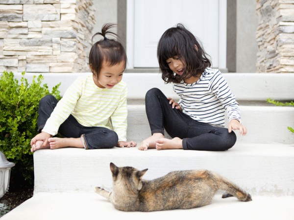 Sisters (2-3, 4-5) sitting in front of house with cat. Photo: Jessica Peterson