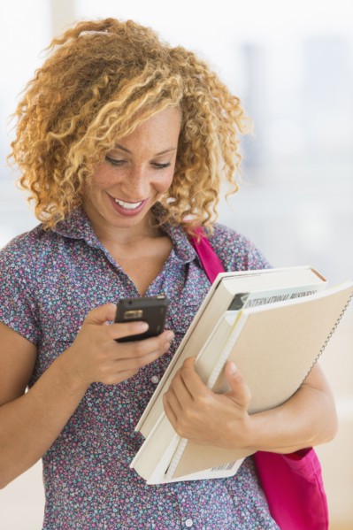 Young woman carrying books and using mobile phone.