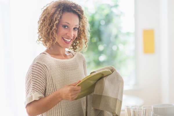 Young woman drying plates in kitchen.