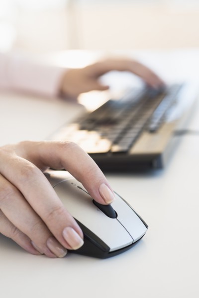 Close up of woman's hands using computer keyboard and computer mouse.