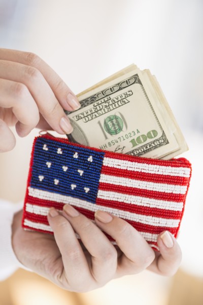 Woman holding banknotes and purse with american flag on it.