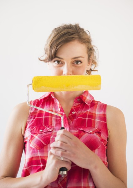Studio shot of young woman holding paint roller. Photo : Daniel Grill