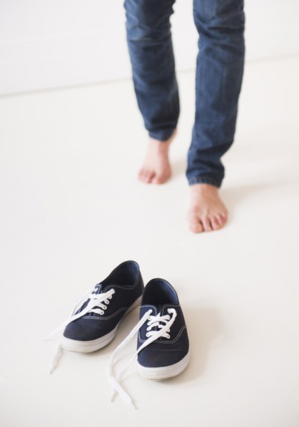 Studio shot of young barefoot woman standing next to shoes, low section. Photo: Daniel Grill