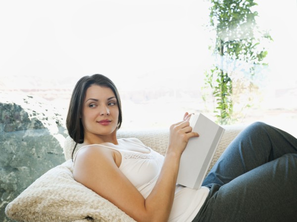 Young attractive woman reading book while sitting on sofa.