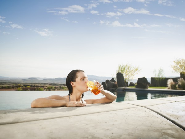 Young attractive woman enjoying cocktail on edge of swimming pool.