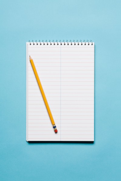 Single yellow sharpened pencil with blank stenographer notebook on blue background. Photo: Kristin