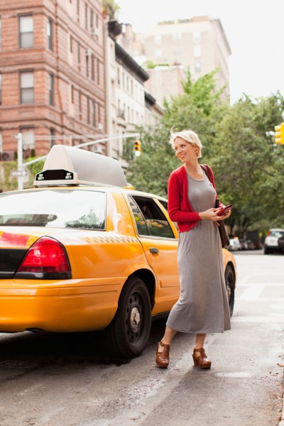 Woman standing next to yellow taxi on street. Photo : Jessica Peterson