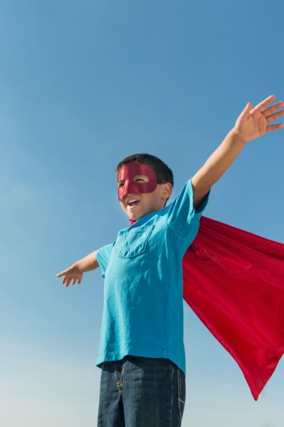 Boy (6-7) in superhero costume under blue sky.