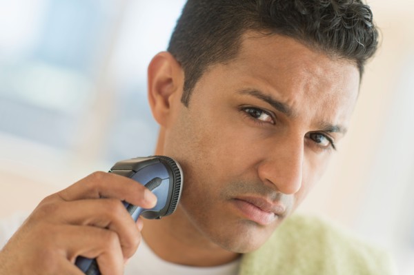 Man shaving with electric razor.