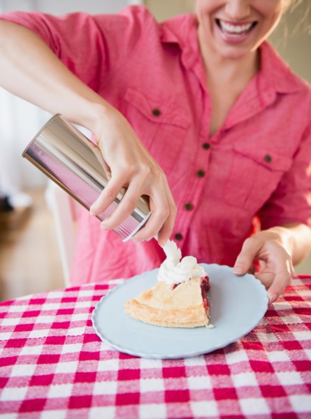 Young woman applying whipped cream on cherry pie