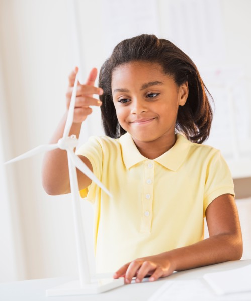 Smiling girl (6-7) playing with wind turbine model