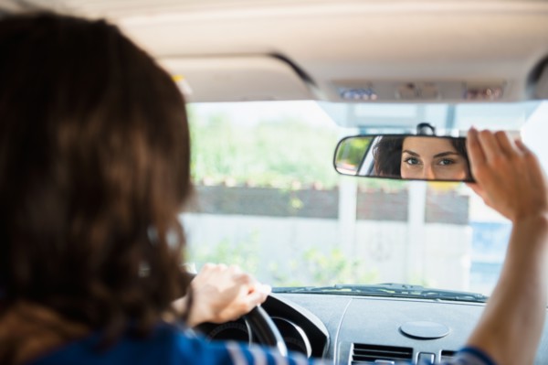 Woman adjusting rear view mirror in car. Photo : Jamie Grill