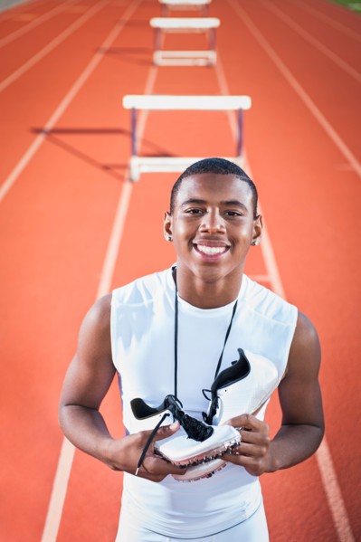 Portrait of smiling boy (12-13) leaning on hurdle on running track.