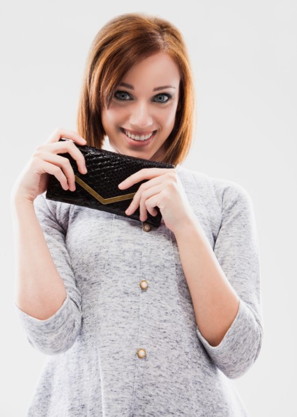 Portrait of young woman showing purse, studio shot. Photo : Mike Kemp