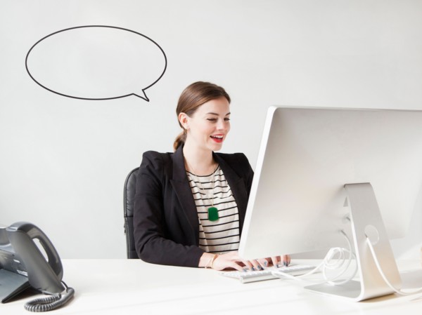 Studio shot of young woman working on computer with speech bubble next to her head. Photo : Jessica