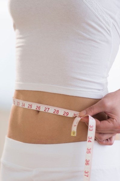 Midsection of woman measuring waistline.