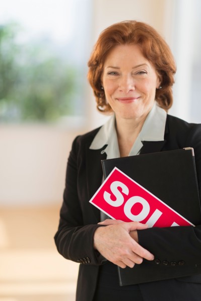 Portrait of female real estate agent holding sold sign.