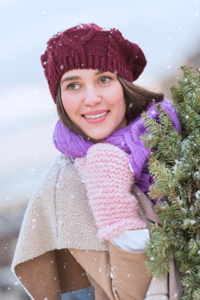 Portrait of young woman wearing knit hat, gloves and scarf an carrying fir wreath.