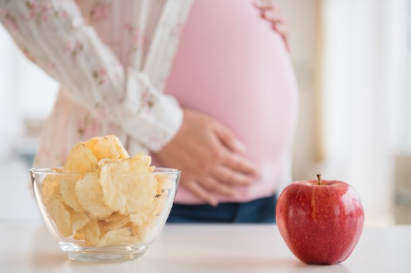 Pregnant woman choosing between apple and chips