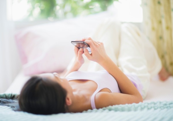 View of Teenage girl ( 16-17 years) using mobile phone lying on bed