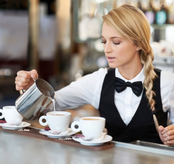 Female barista pouring milk into coffee cup