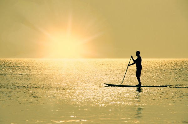 Man standing on paddle board at sunset