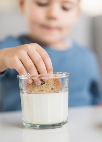 Boy (4-5) dipping cookie in milk.
