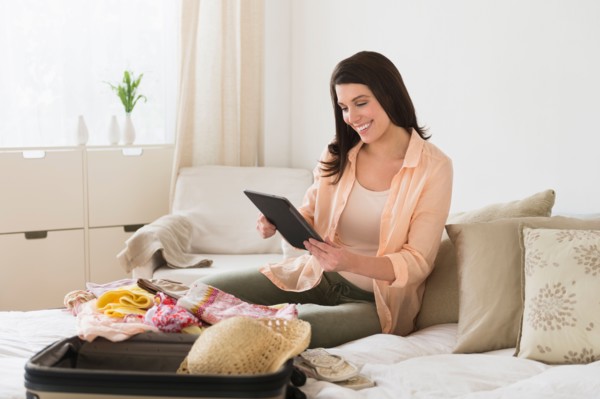 Woman using digital tablet while packing suitcase.