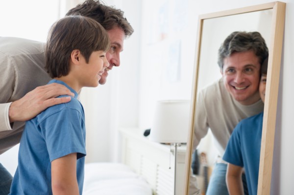 Father and son (8-9) looking into mirror