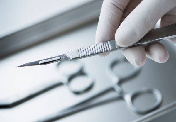Close up of hand in surgical glove holding dental scalpel, studio shot.