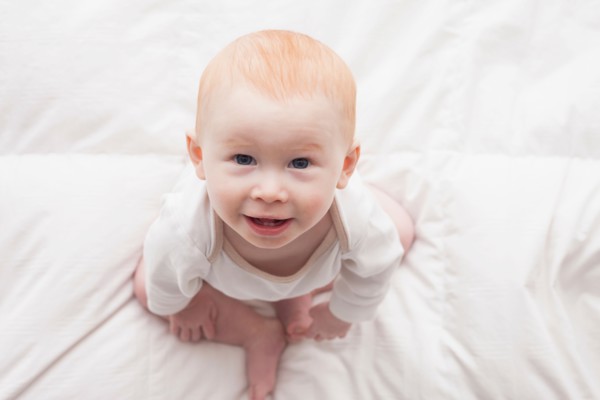 Directly above portrait of baby boy (18-23 months) sitting on duvet and looking at camera
