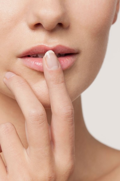 Studio shot portrait of young woman in white blouse with finger on lips