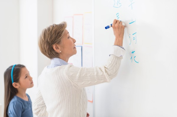 Teacher and schoolgirl (8-9) writing at whiteboard.