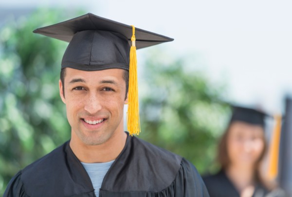 Portrait of male student on graduation ceremony with female student in background.