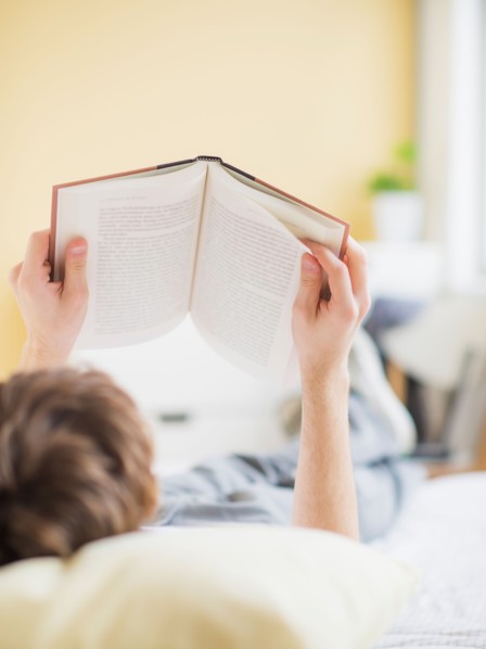 Teenage boy (14-15) lying on bed and reading book