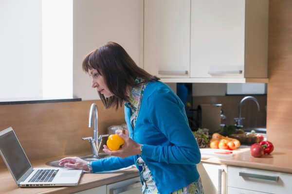 Mature woman using laptop while cooking
