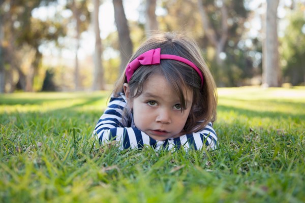 Portrait of sad girl (4-5 years) lying on grass in park