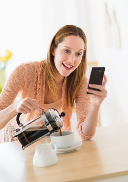 Woman pouring coffee and looking at phone.