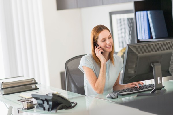 Business woman using computer and phone in office.