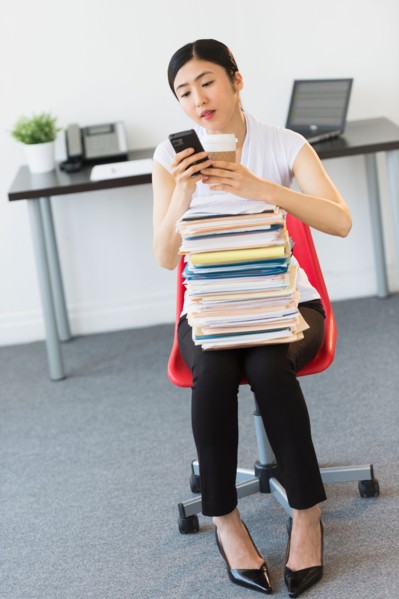 Businesswoman with stack of files texting on phone.