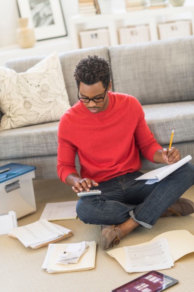 Man sitting on floor in living room and calculating bills.