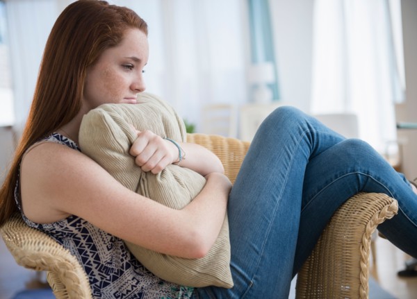 Teenage girl (14-15) sitting sad in armchair