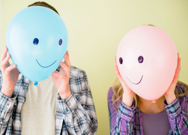 Studio shot of couple holding balloons with smiley faces in front of their heads