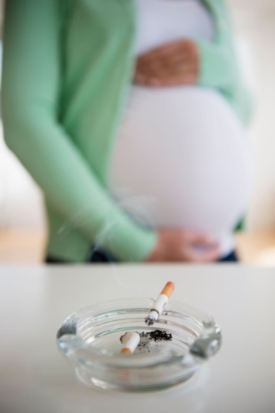 Mid section of pregnant woman, ashtray and cigarette in front