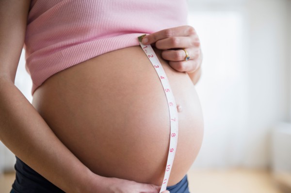 Mid section of pregnant woman measuring her belly
