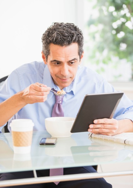 View of mature man eating cereal and using digital tablet