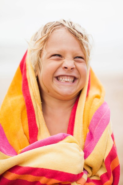 Boy (6-7) wrapped in towel on beach